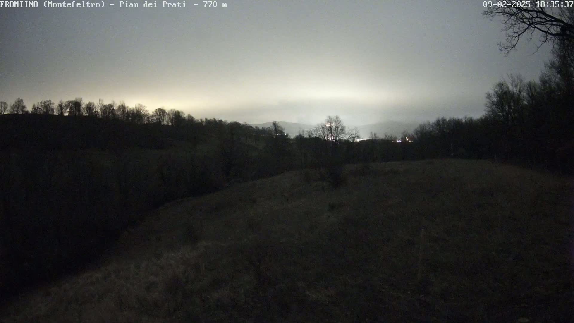A dark, hilly landscape is visible under a cloudy, twilight sky.