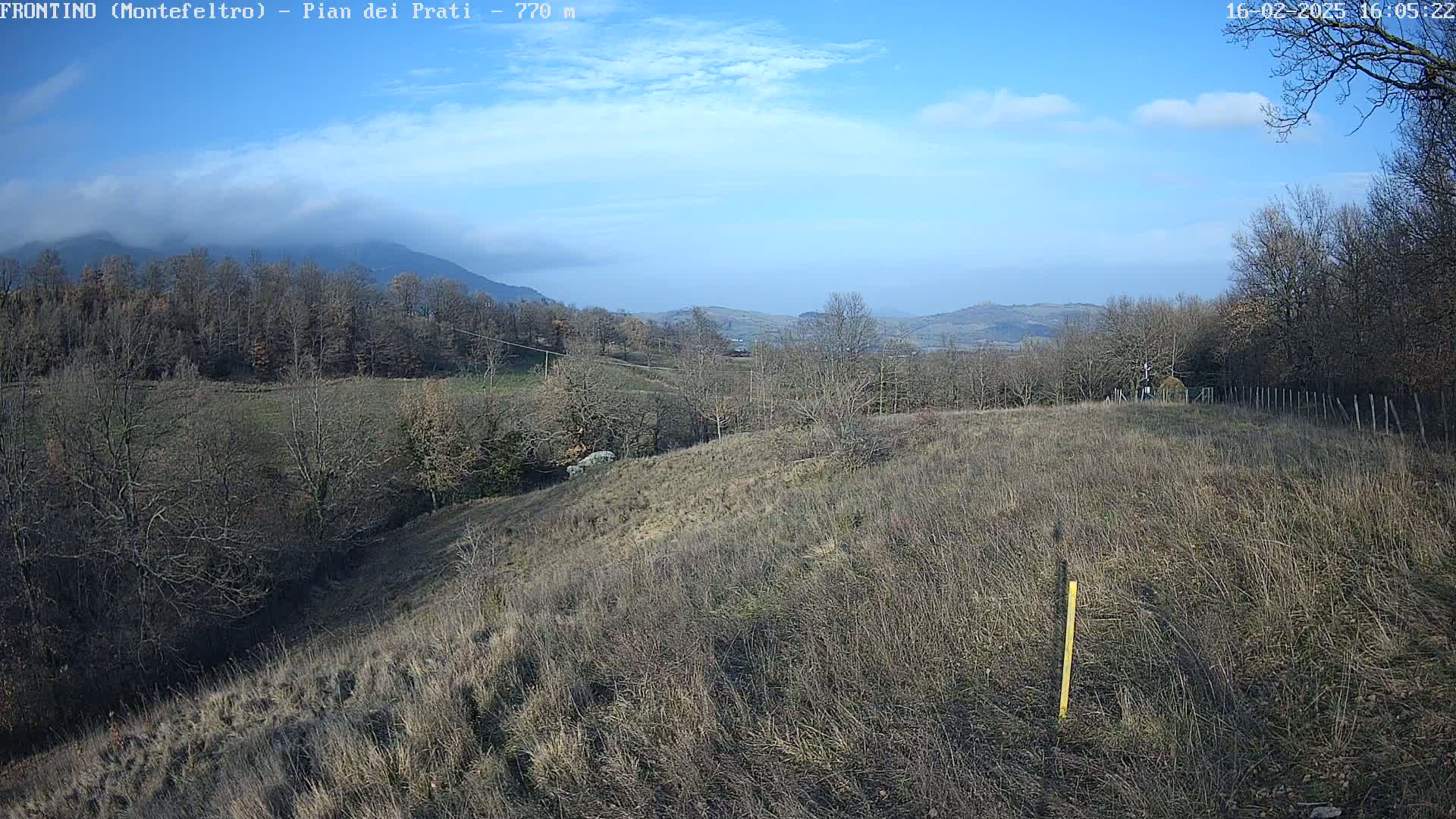 A mostly clear, sunny day reveals a hilly landscape with leafless trees and dry, brown grass under a partly cloudy sky.