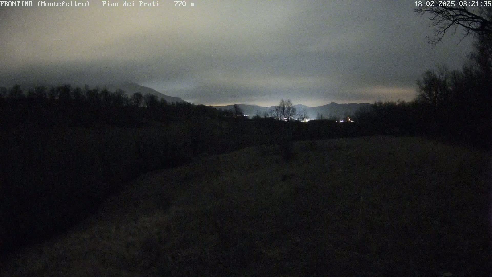 A nighttime view of dark hills and distant lights under a cloudy sky.