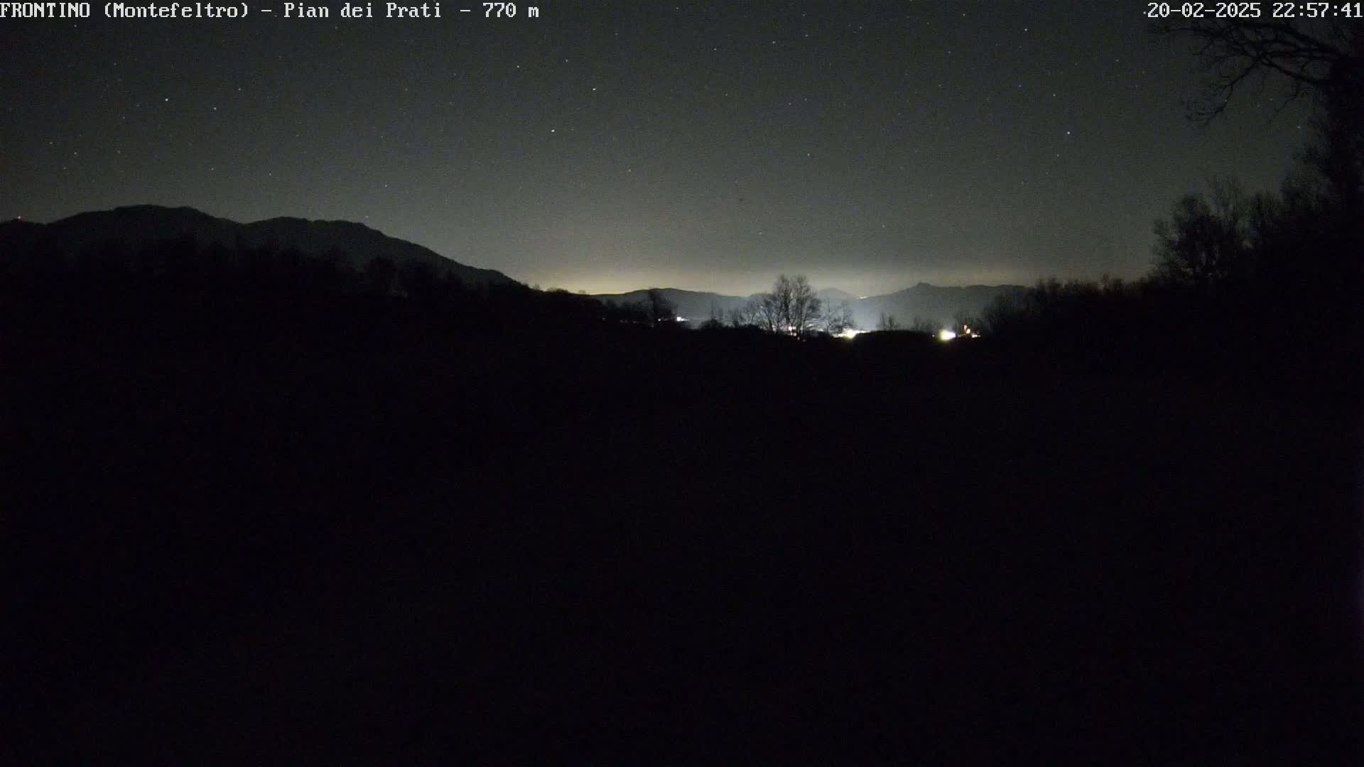 A nighttime view of a dark landscape with distant mountains under a clear, starry sky.