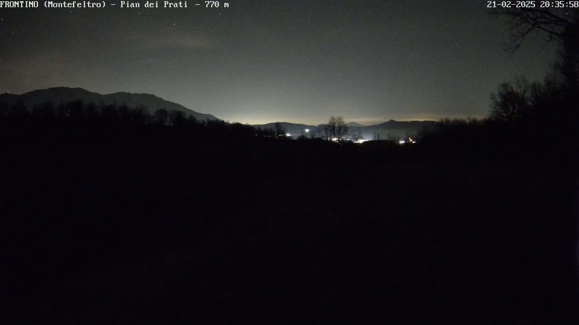 A nighttime, dark landscape shows silhouetted trees and mountains under a clear, starlit sky.