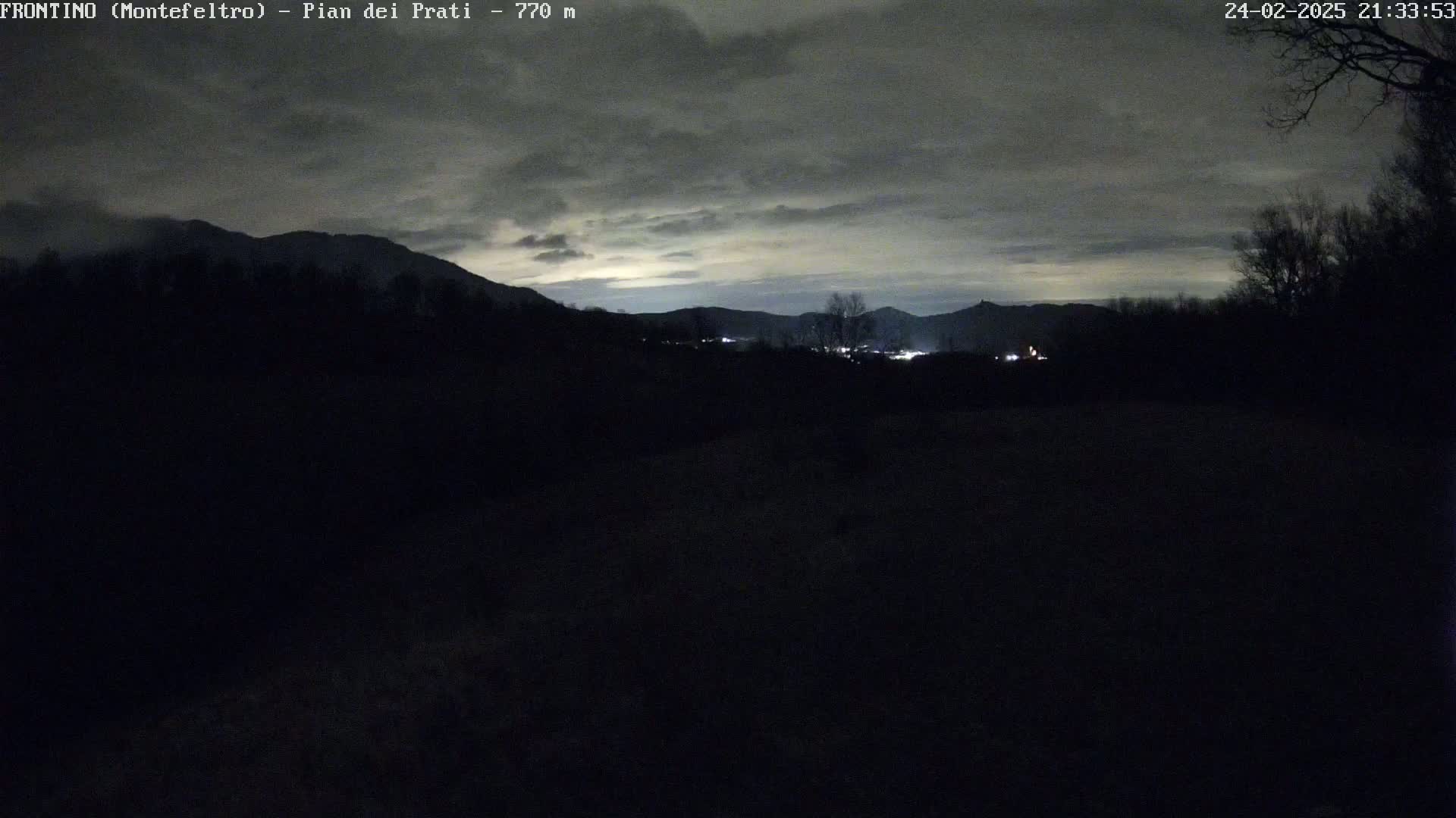A nighttime view of dark, silhouetted hills and trees under a cloudy sky.
