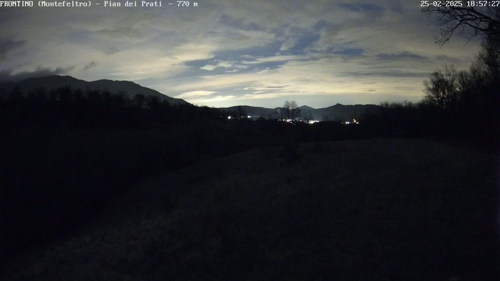 A dark, nighttime landscape shows silhouetted mountains and trees under a cloudy, twilight sky.