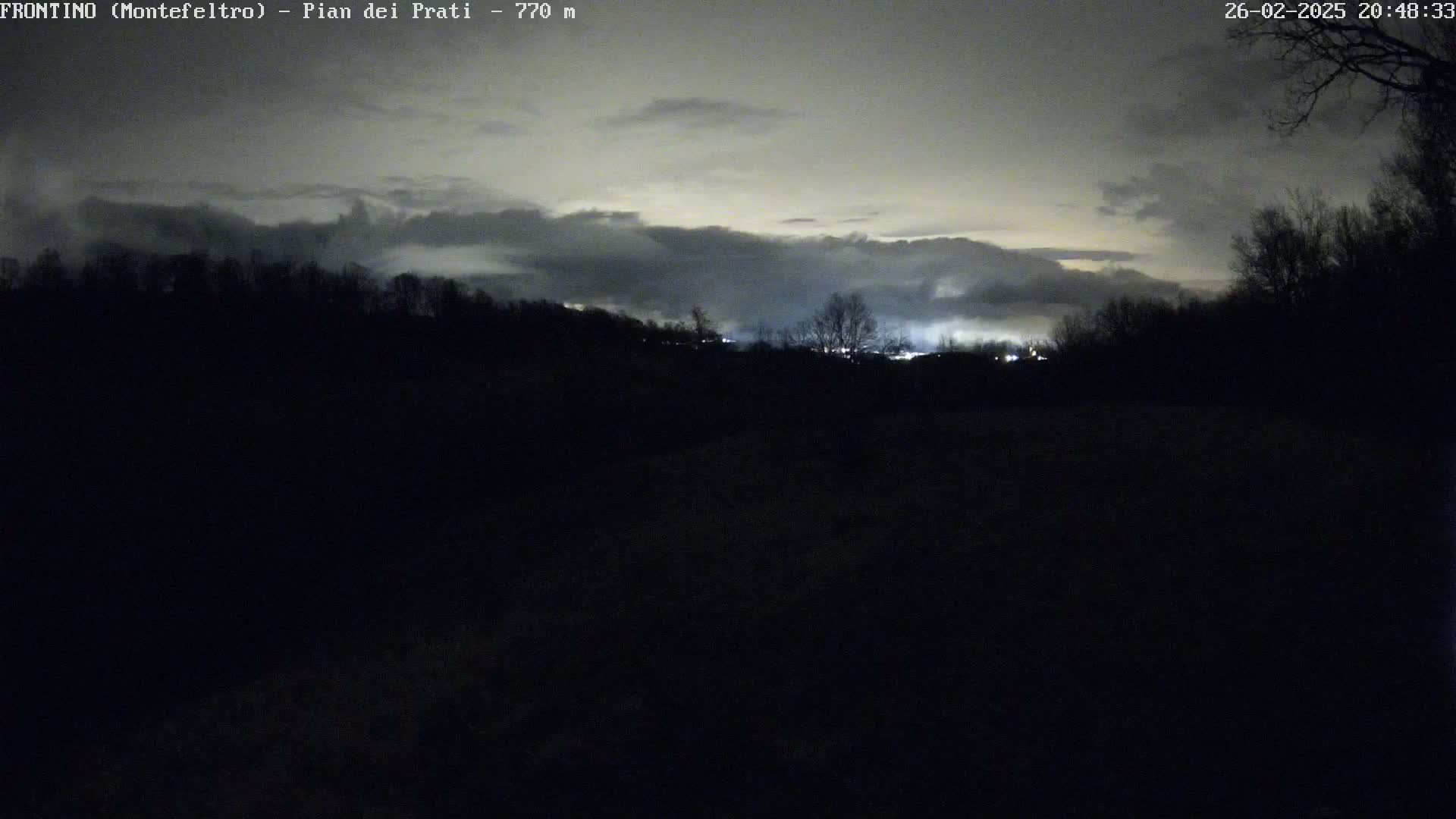A nighttime, overcast scene shows a dark, silhouetted landscape with faintly lit areas in the distance.