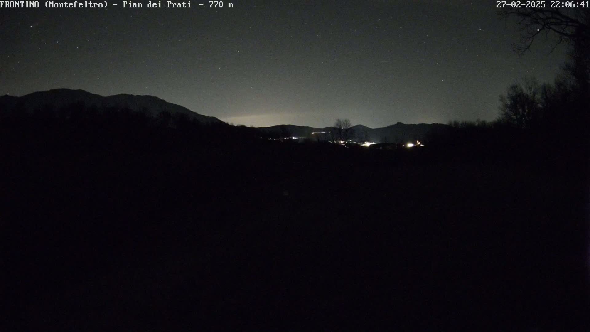 A nighttime view of a dark, silhouetted landscape featuring mountains under a starry sky.