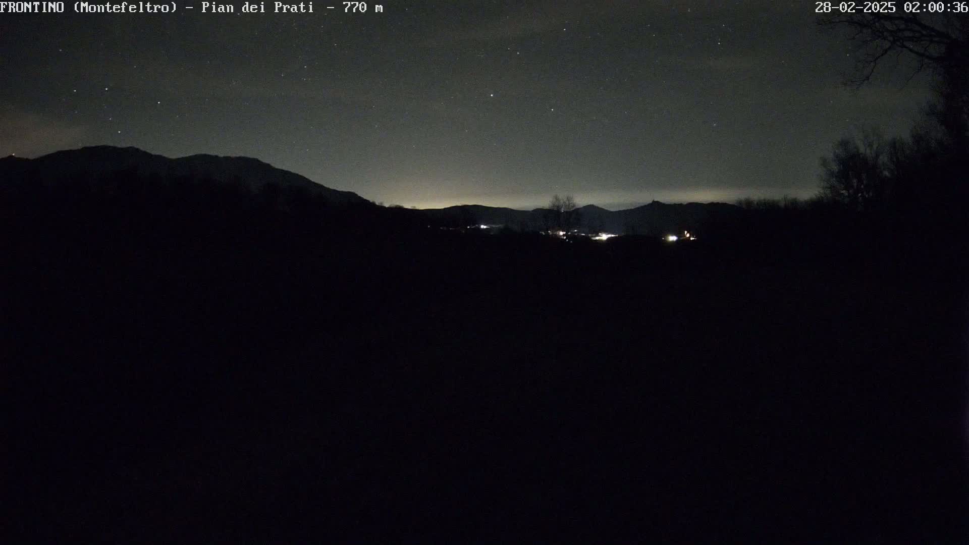 A dark, nighttime landscape shows a silhouetted mountain range under a clear, starry sky.