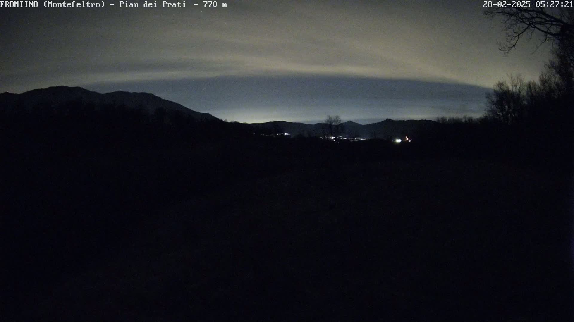 A dark, nighttime landscape shows silhouetted mountains under a cloudy, dusky sky.