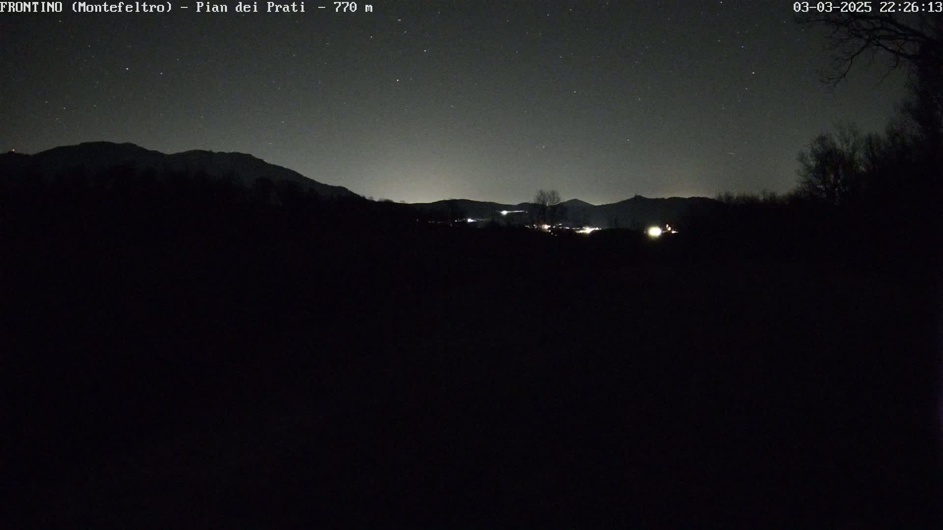 A nighttime view of a dark landscape with distant mountains under a clear, starry sky.