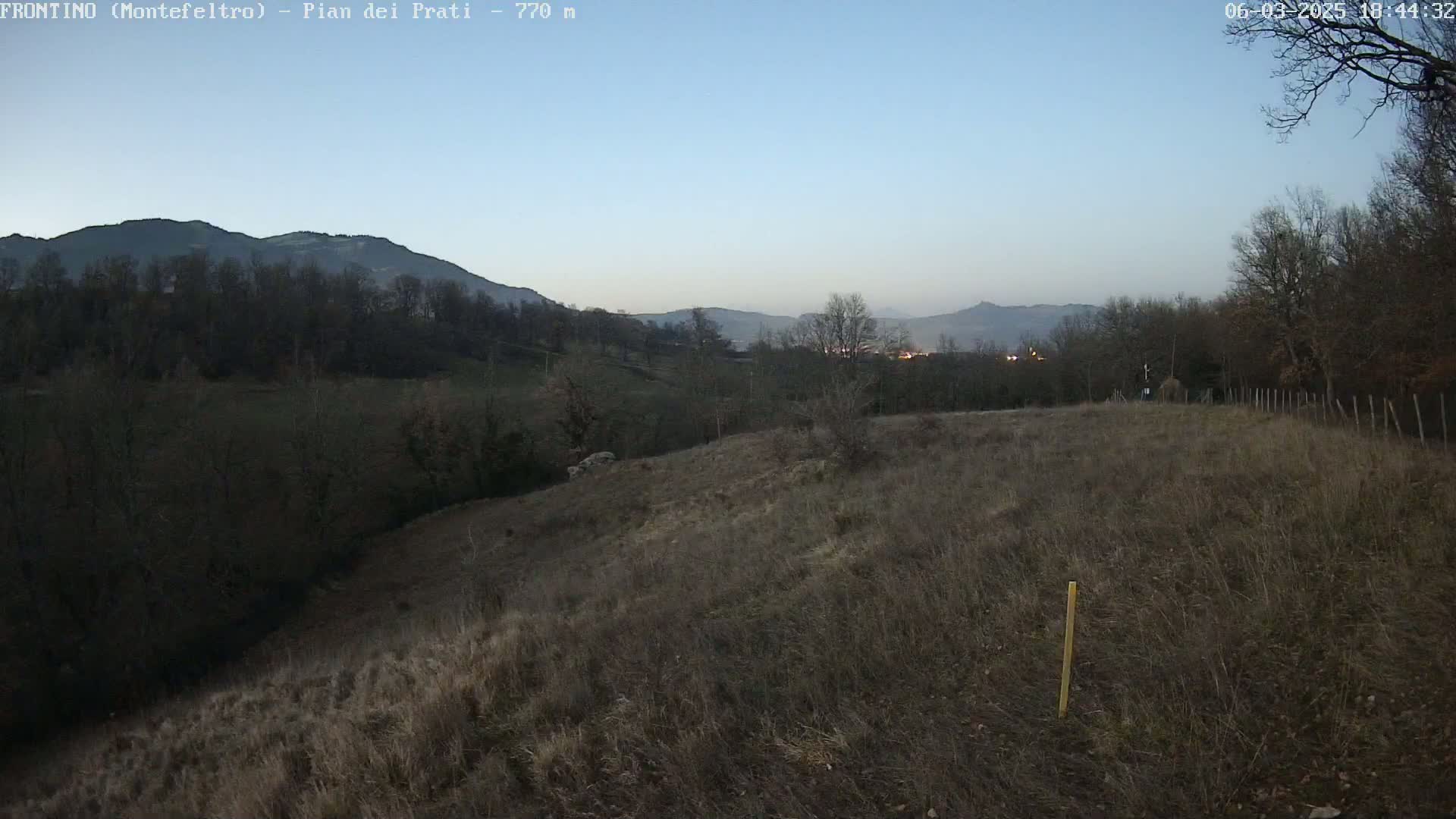 A brown, grassy hillside under a twilight sky overlooks a valley of dark trees and distant hills.