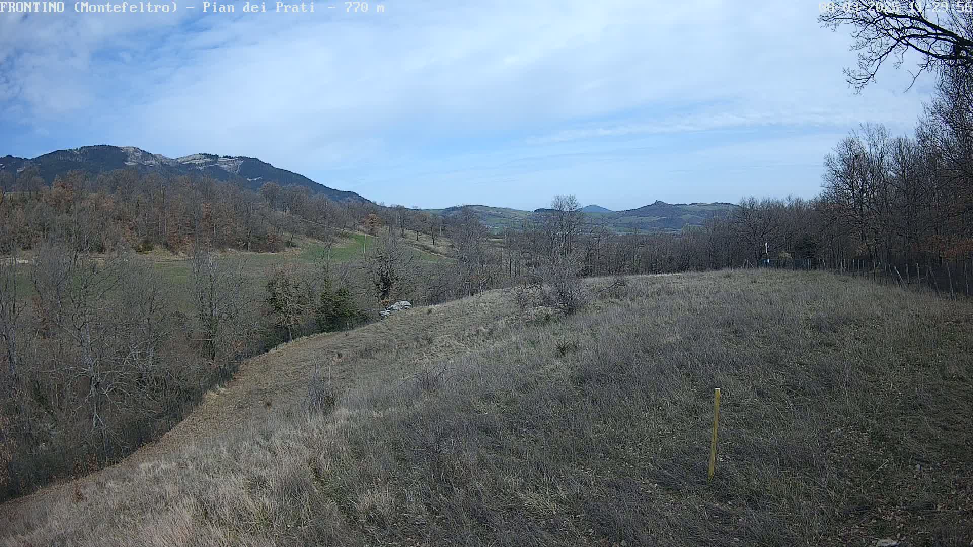A mostly-barren, hilly landscape under a partly cloudy sky stretches to distant mountains.