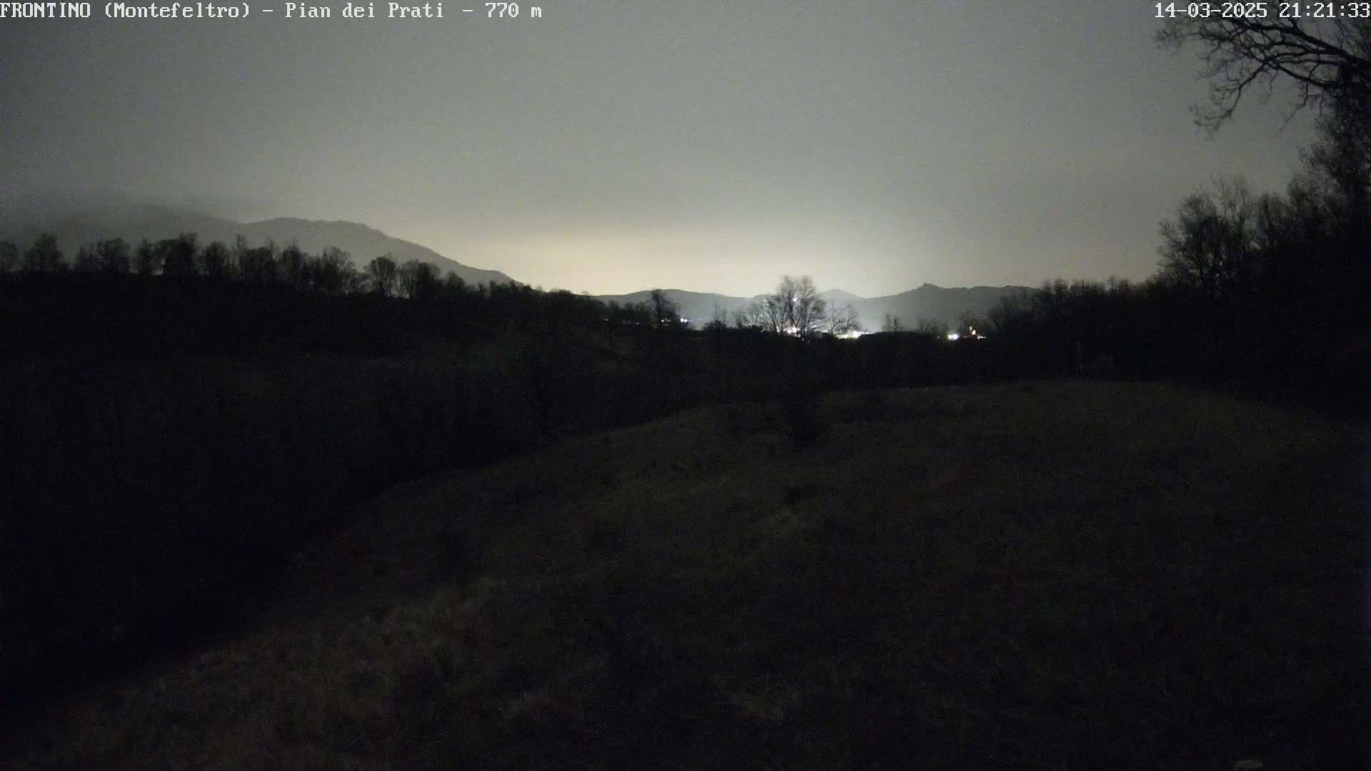 A dark, nighttime landscape shows silhouetted trees and hills under a dim, gray sky.