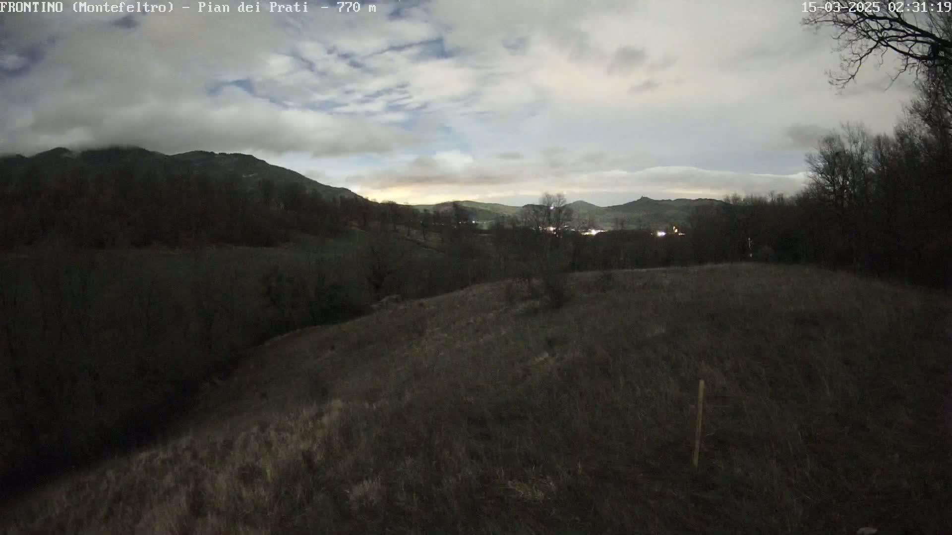 A dimly lit, hilly landscape under a cloudy, twilight sky is visible from an elevated vantage point.