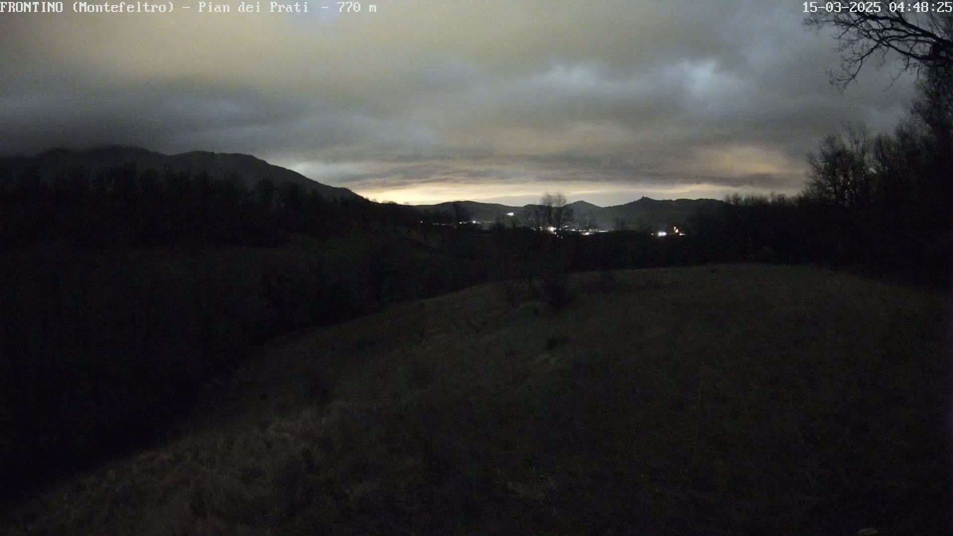 A dark, hilly landscape is visible under a mostly cloudy, twilight sky.