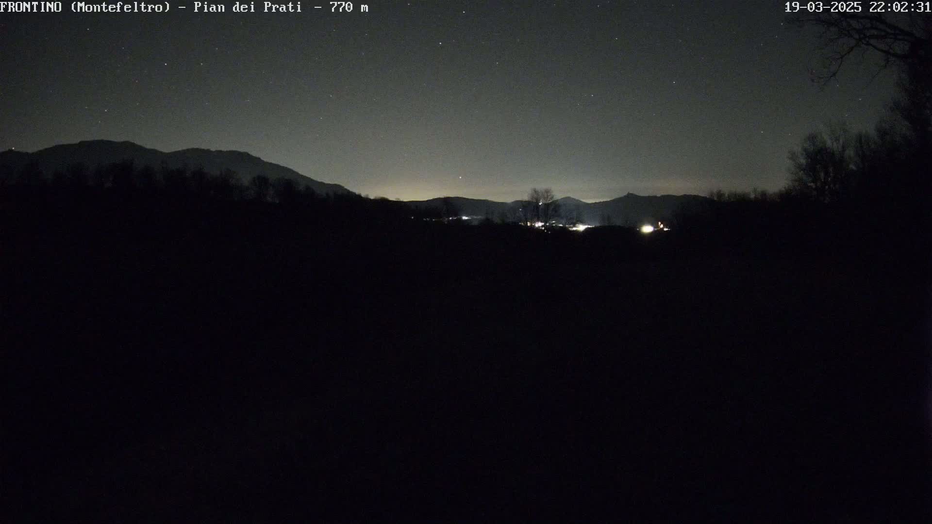 A nighttime view of dark, silhouetted mountains under a clear, starry sky.