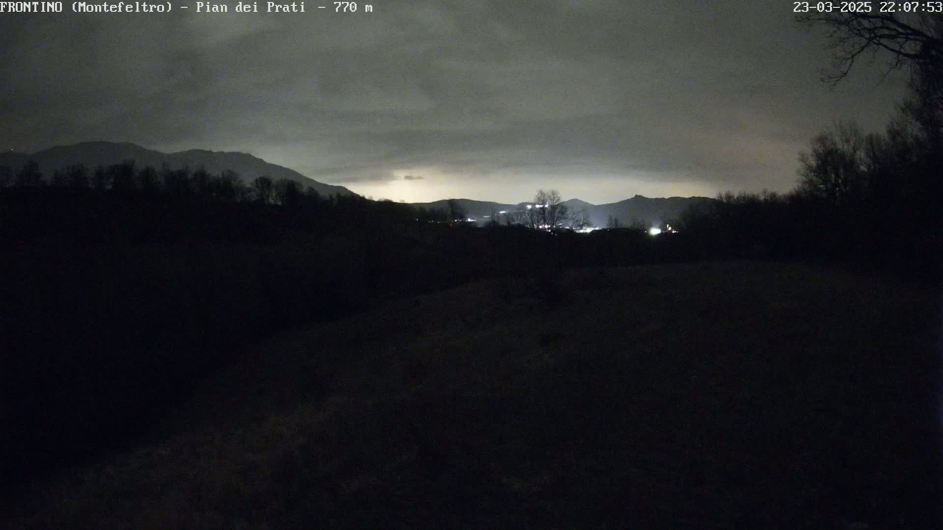 A nighttime view of dark, silhouetted hills and trees under a cloudy sky.