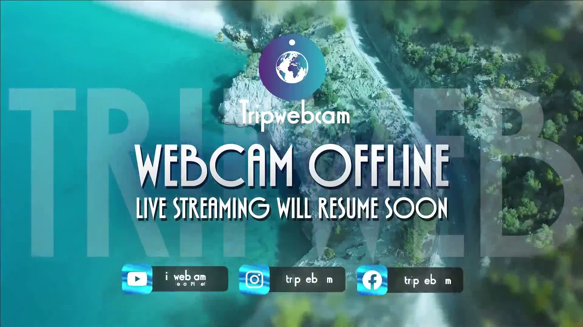 An aerial view of a coastline with turquoise water and green land shows a message that the webcam is offline and will resume soon.