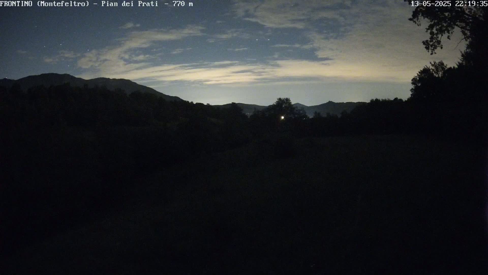 A nighttime view of dark, silhouetted hills under a partly cloudy sky with some stars visible.