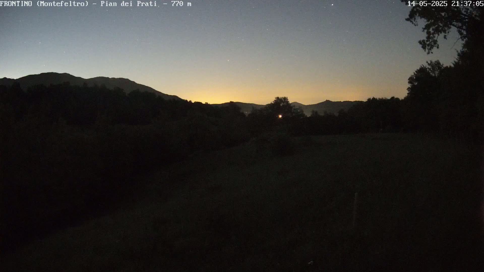A twilight view shows a dark, silhouetted landscape of trees and distant mountains under a clear, star-studded sky.