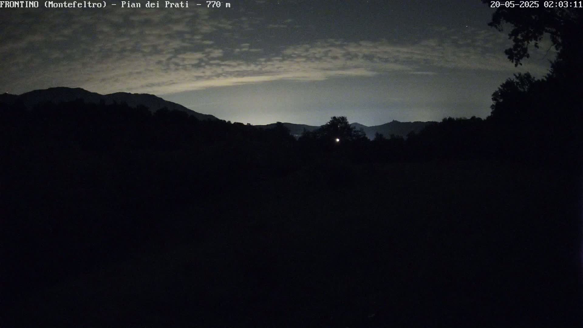 A nighttime view shows dark silhouetted mountains under a cloudy sky.