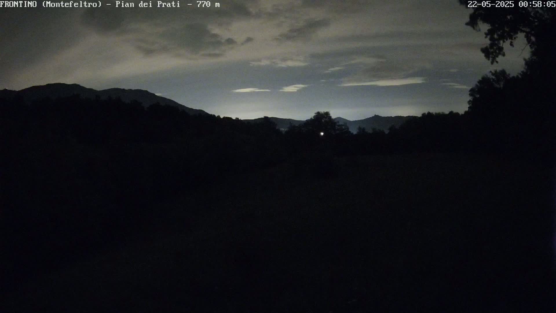 A dark, nighttime landscape shows silhouetted mountains under a cloudy sky.