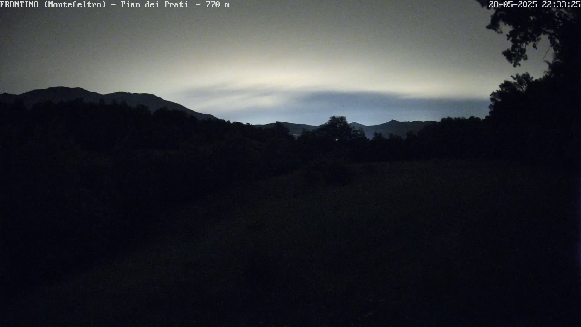A dark, nighttime landscape shows silhouetted mountains under a pale, cloudy sky.