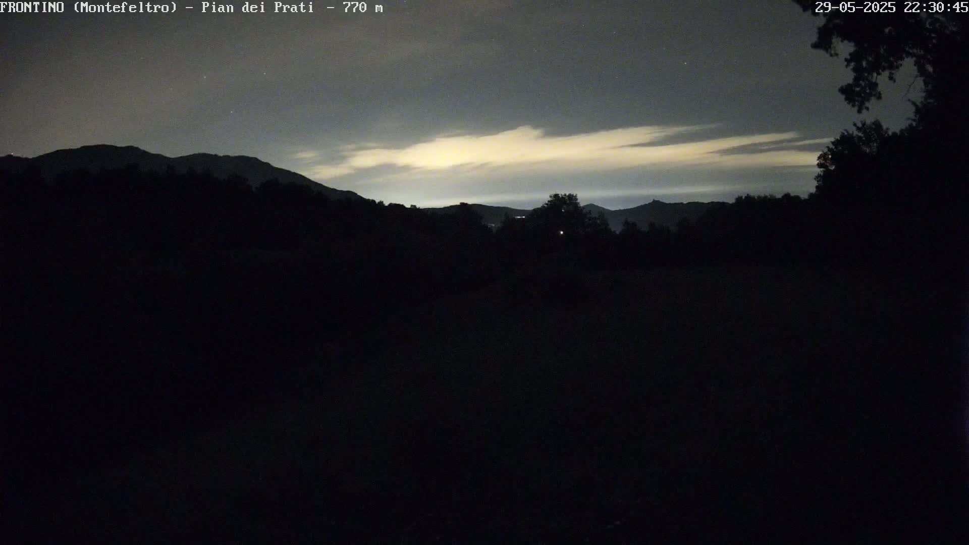 Silhouetted mountains are visible under a night sky with a thin layer of clouds illuminated by a faint light source.