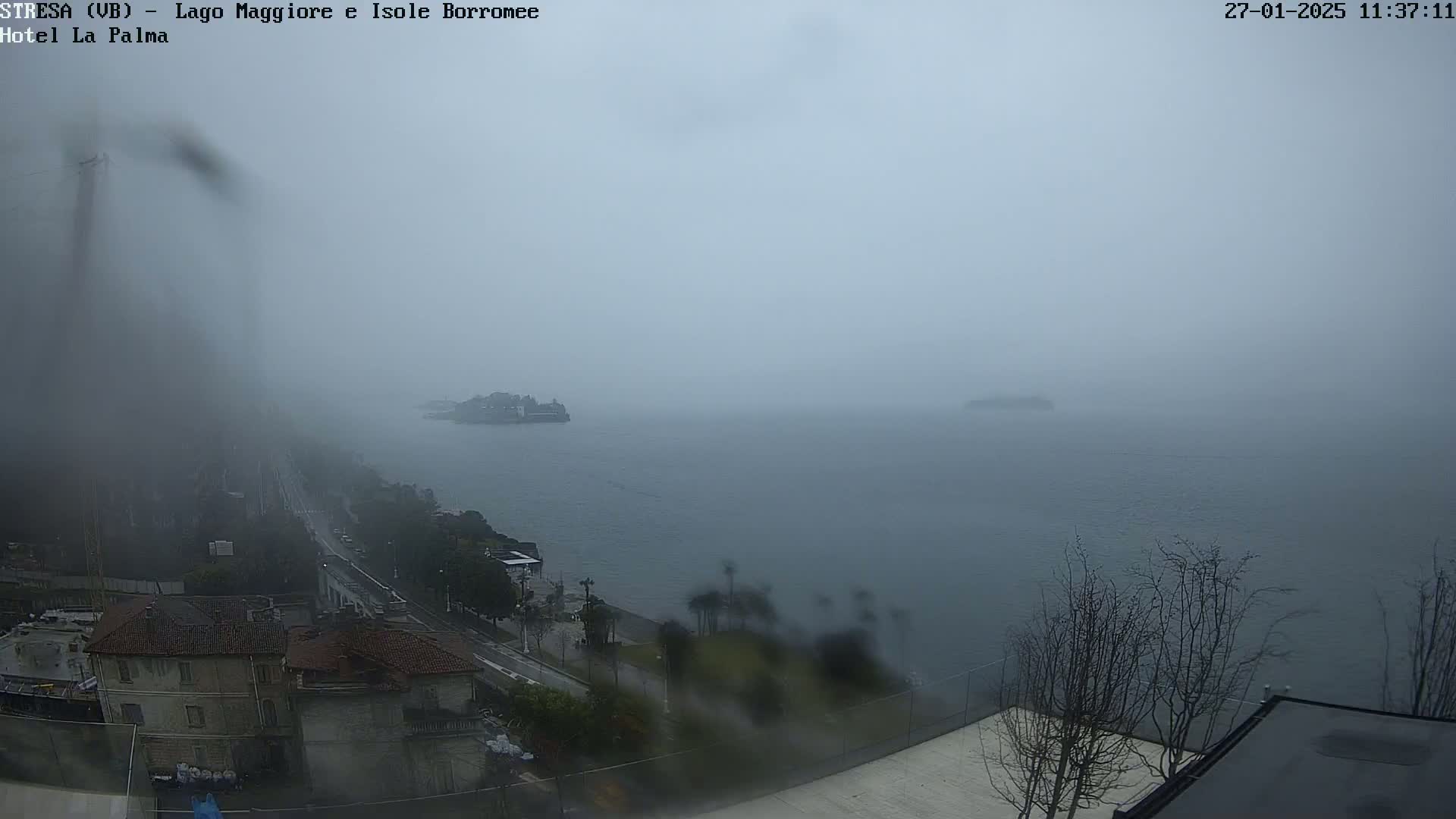 A hazy, rainy view of a lake and shoreline, with buildings visible in the foreground.