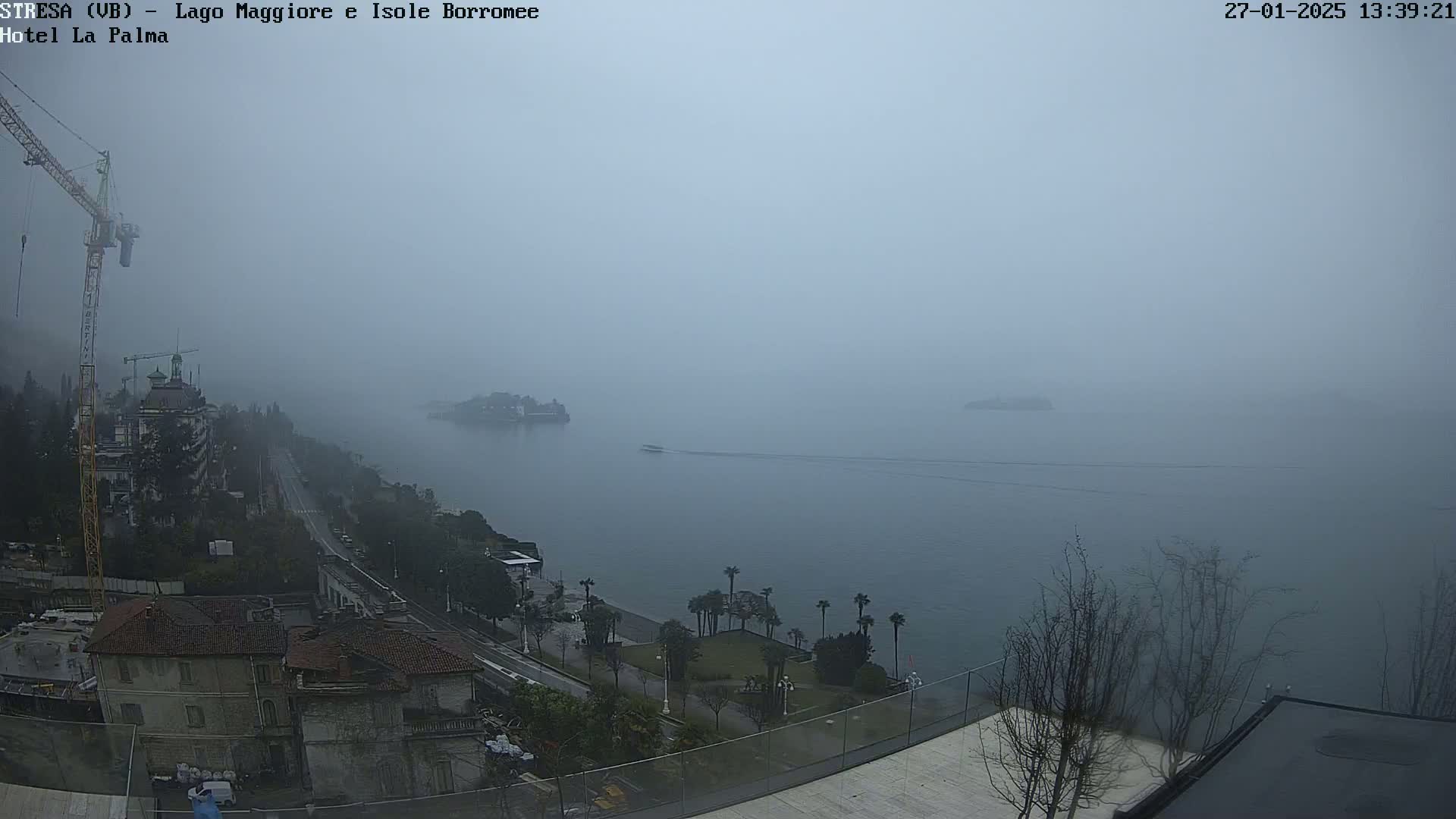 A foggy view of a lake, with buildings and a construction crane visible on the shore.