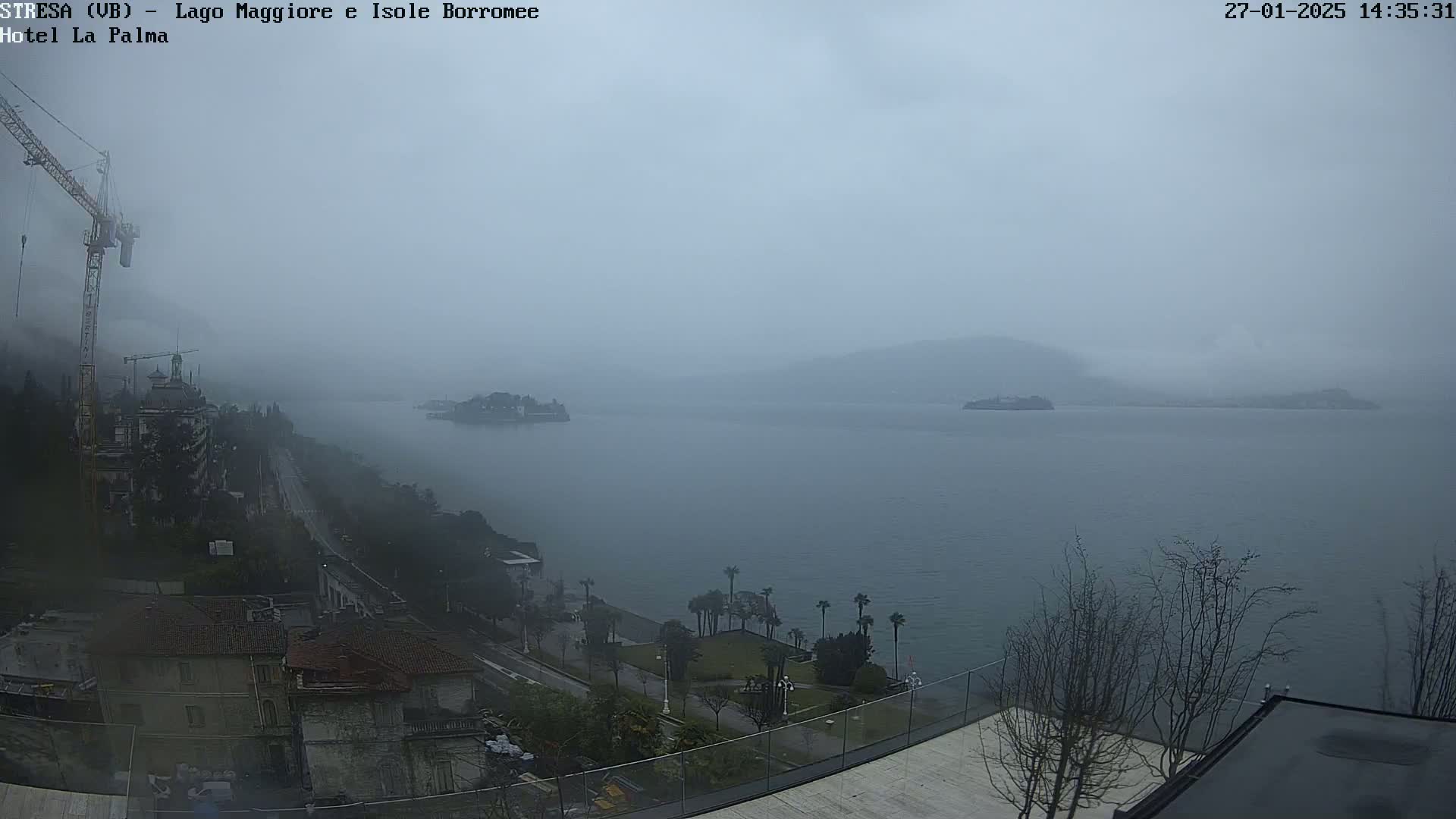 A misty, overcast view of a lake with distant islands and a shoreline featuring buildings, trees, and a construction crane.