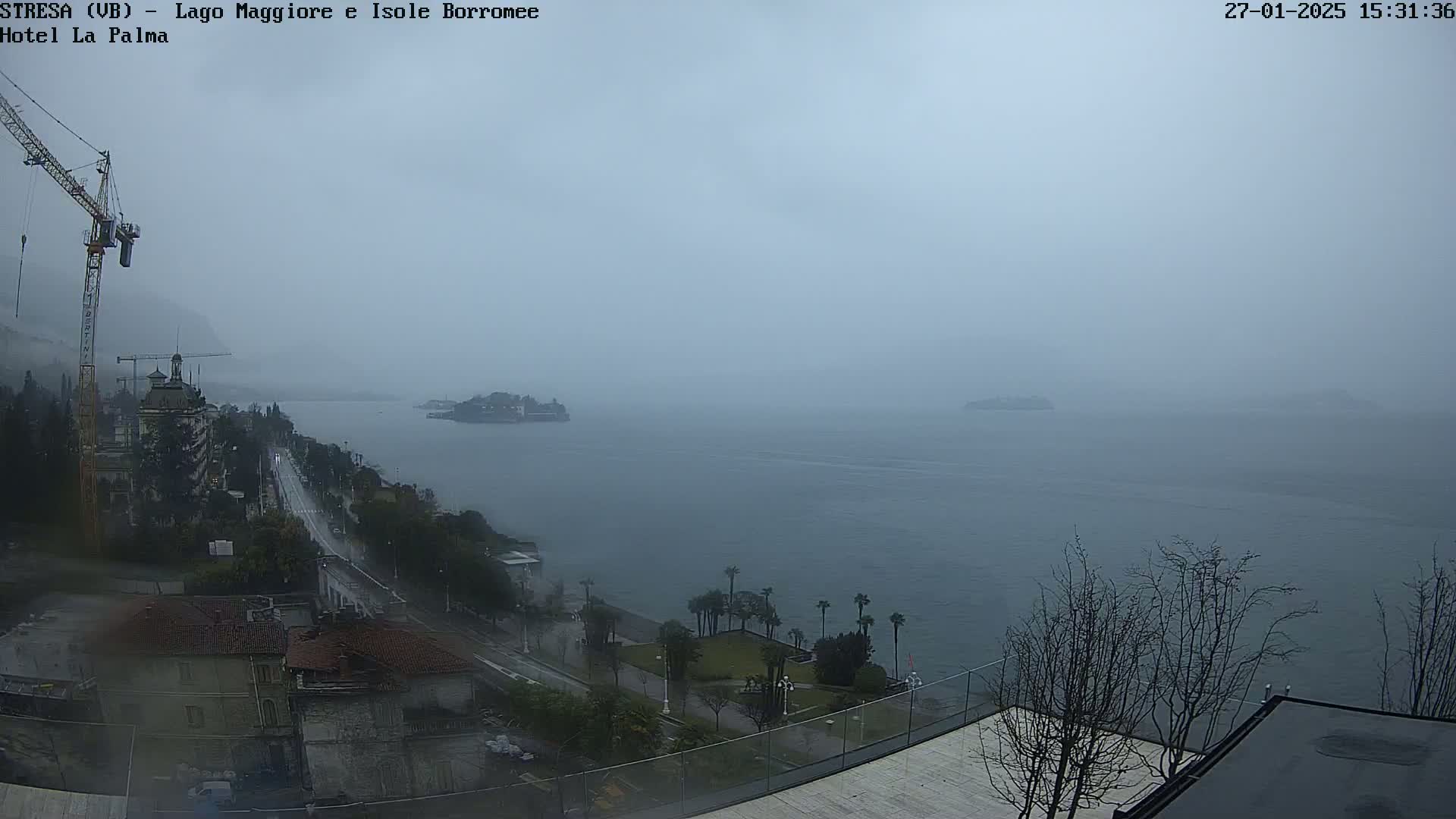 A foggy, overcast day reveals a lake view with a small island in the distance, a coastal road, buildings, and a construction crane.