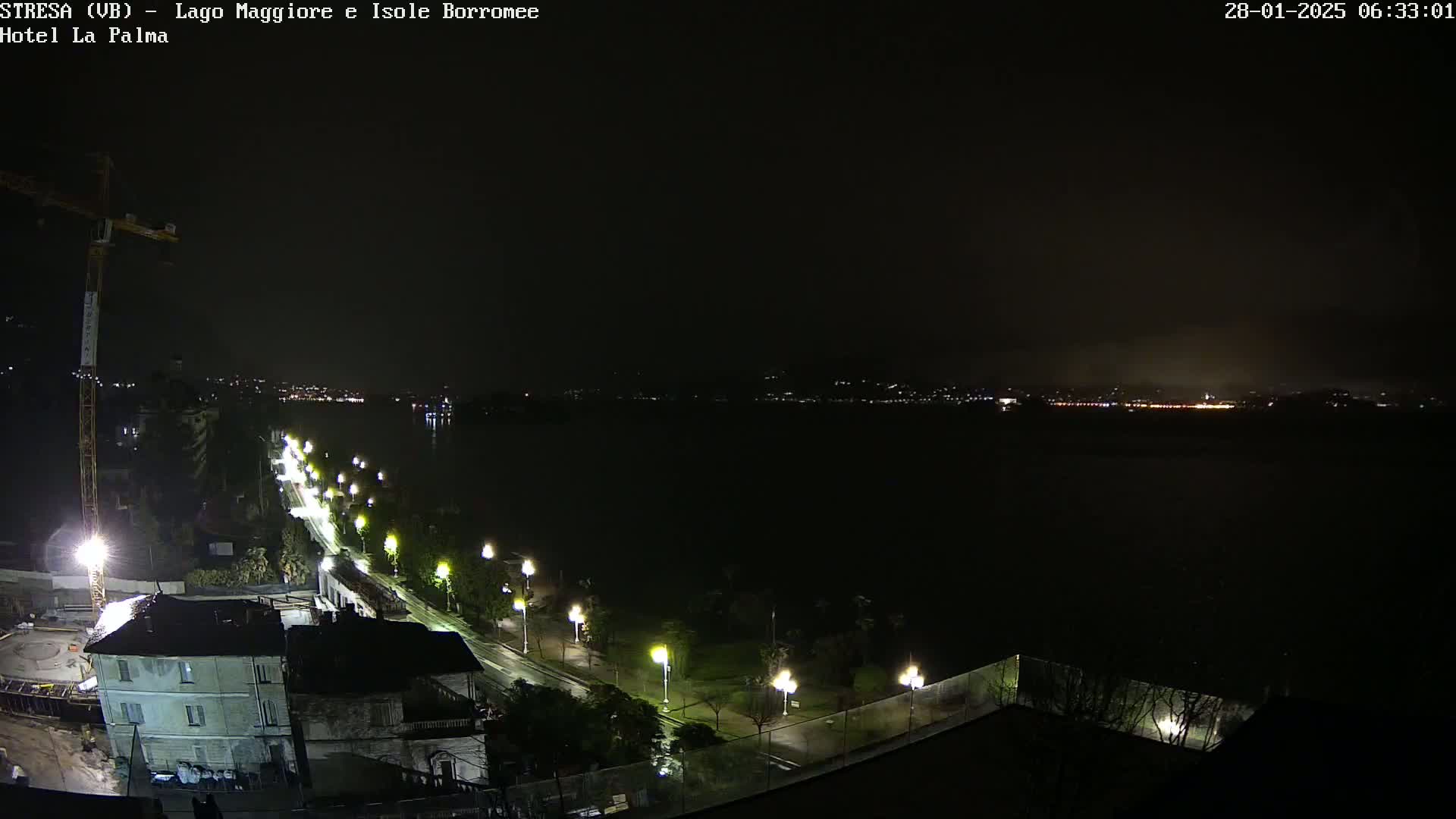 A nighttime view of a lake with a dimly lit road and buildings along its shore under a dark, possibly overcast sky.