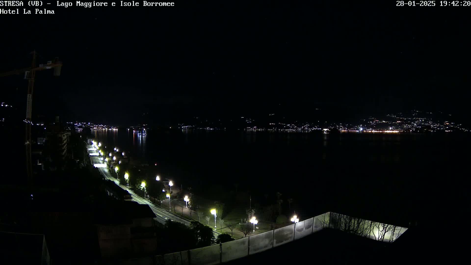 A nighttime view of a city across a calm lake, illuminated by streetlights along a waterfront road.