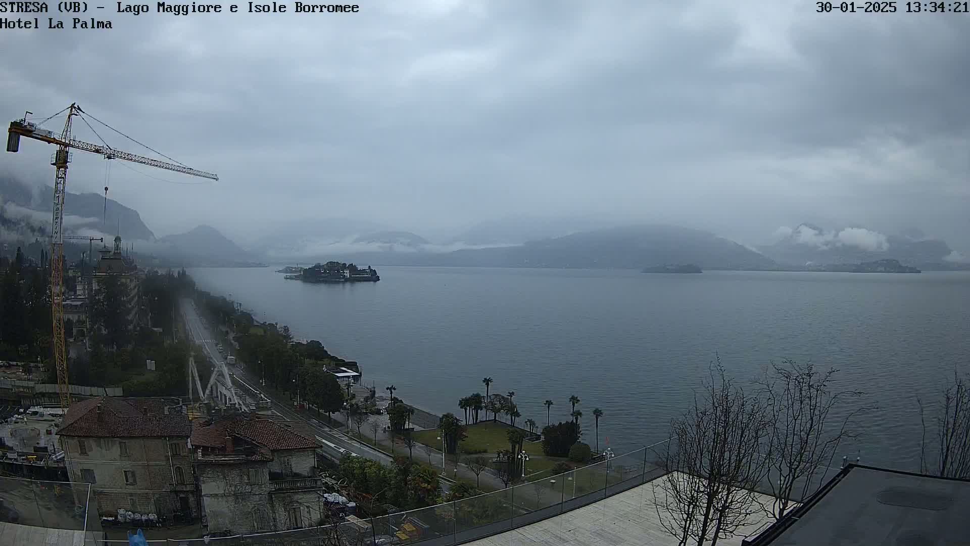 A large body of water is seen under an overcast sky, with a construction crane, buildings, and trees visible along its shoreline.