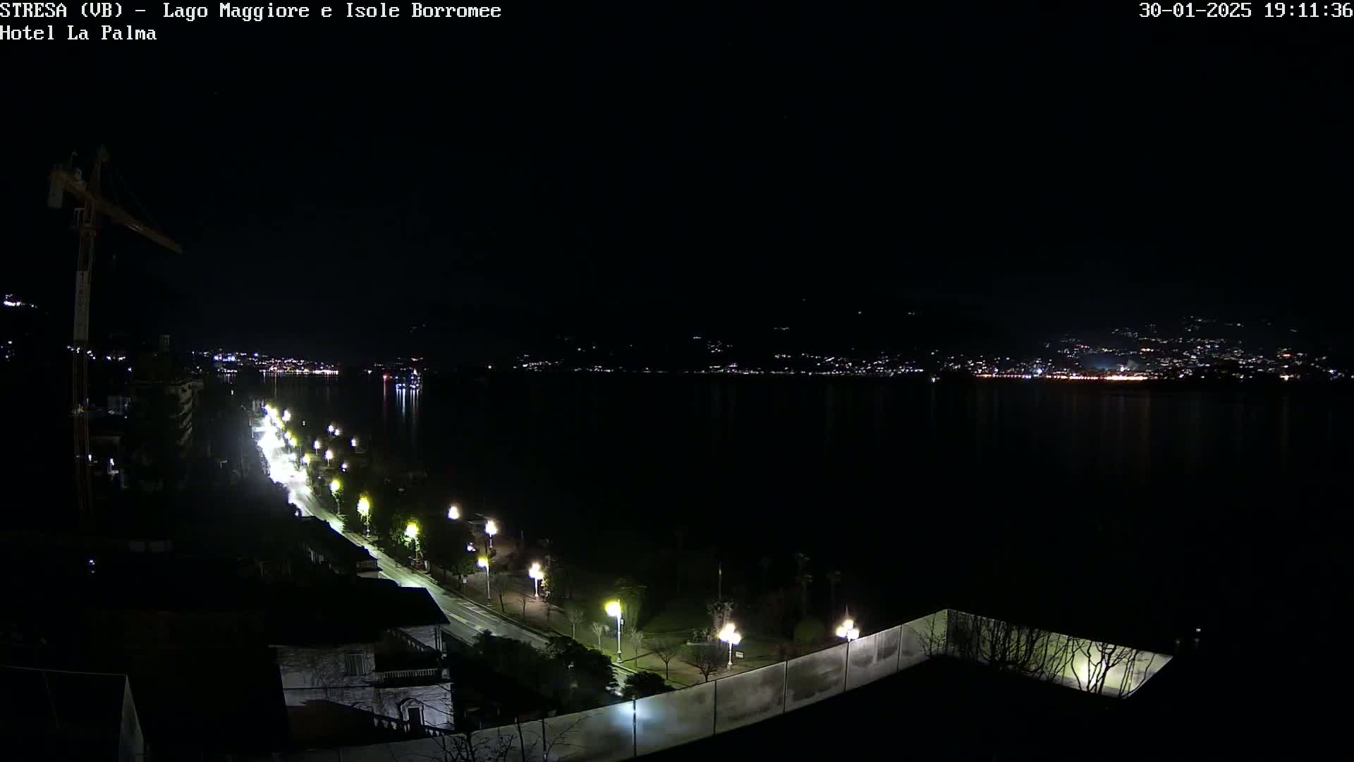 A nighttime view of a city's waterfront illuminated by streetlights, overlooking a dark body of water with distant city lights on the opposite shore.