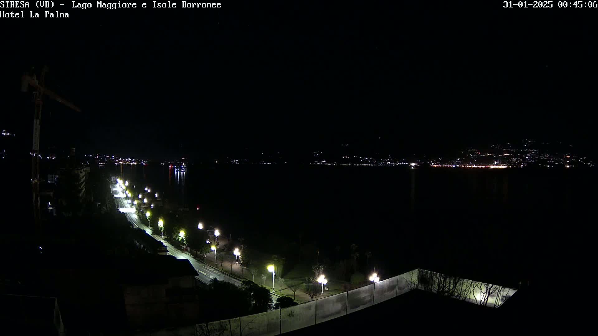 A nighttime view of a dark body of water with a city skyline in the distance, a road lined with streetlights leading down to the water's edge.