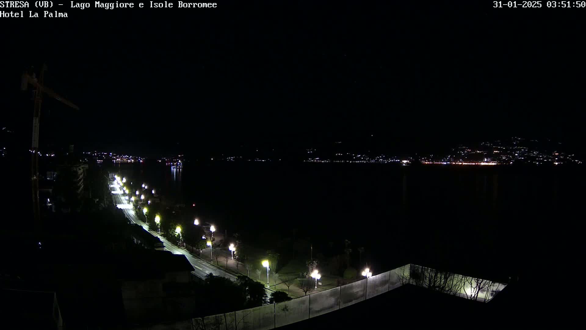 A nighttime, long-range view of a city and lake, illuminated by streetlights along a road that curves toward the water.