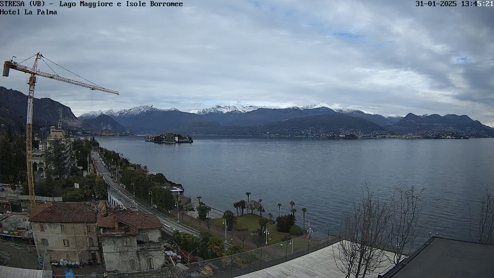 A partly cloudy day overlooking a large lake with snow-capped mountains in the background, a construction crane, and a lakeside town.
