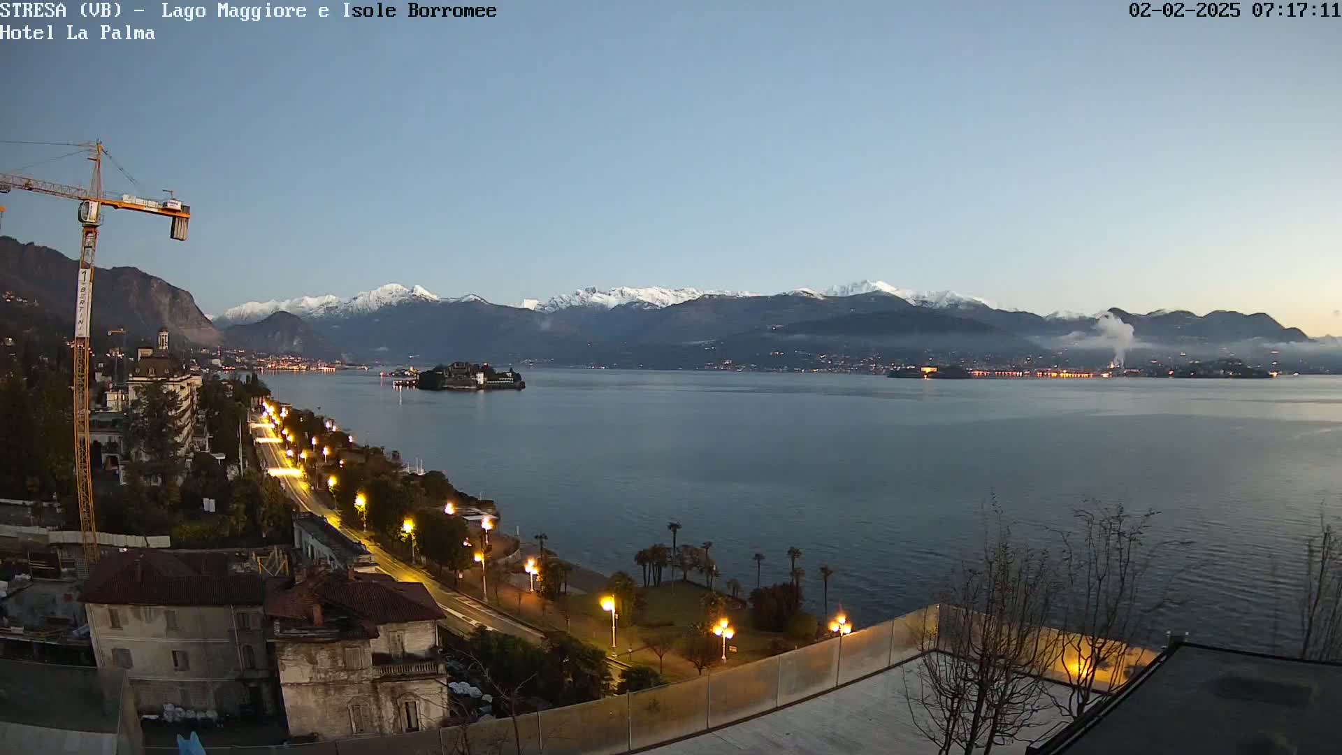 A twilight view of a calm lake, with snow-capped mountains in the background, a city along the shore illuminated by lights, and an island in the middle of the lake.