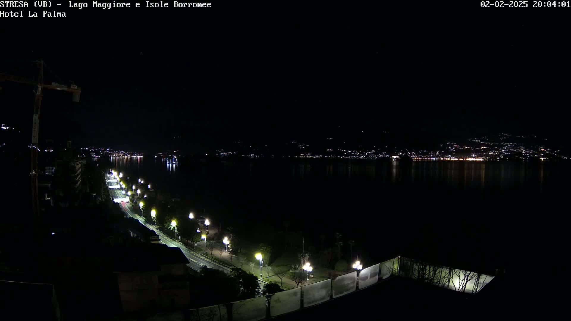 A nighttime view of a city across a calm body of water, with a road lined with lights leading down to the waterfront.