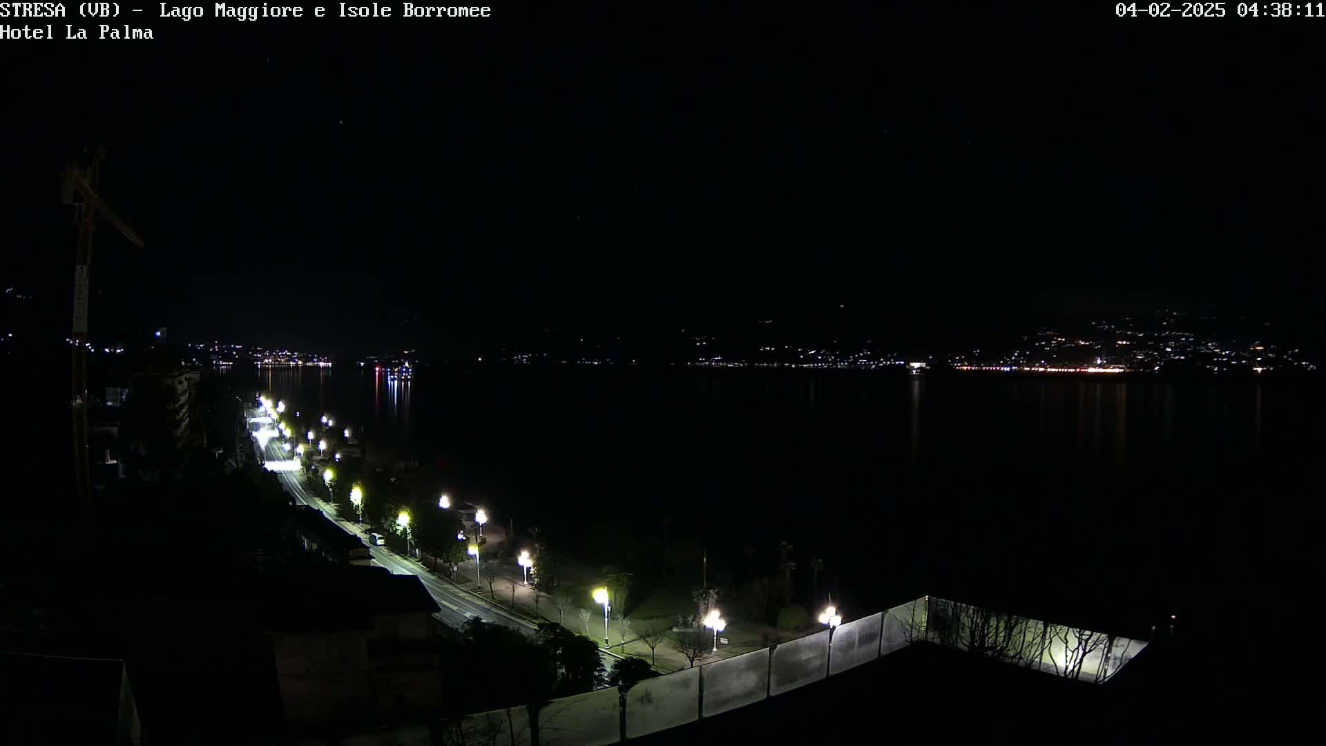 A nighttime view of a city across a body of water, with a lit road curving along the shoreline in the foreground.