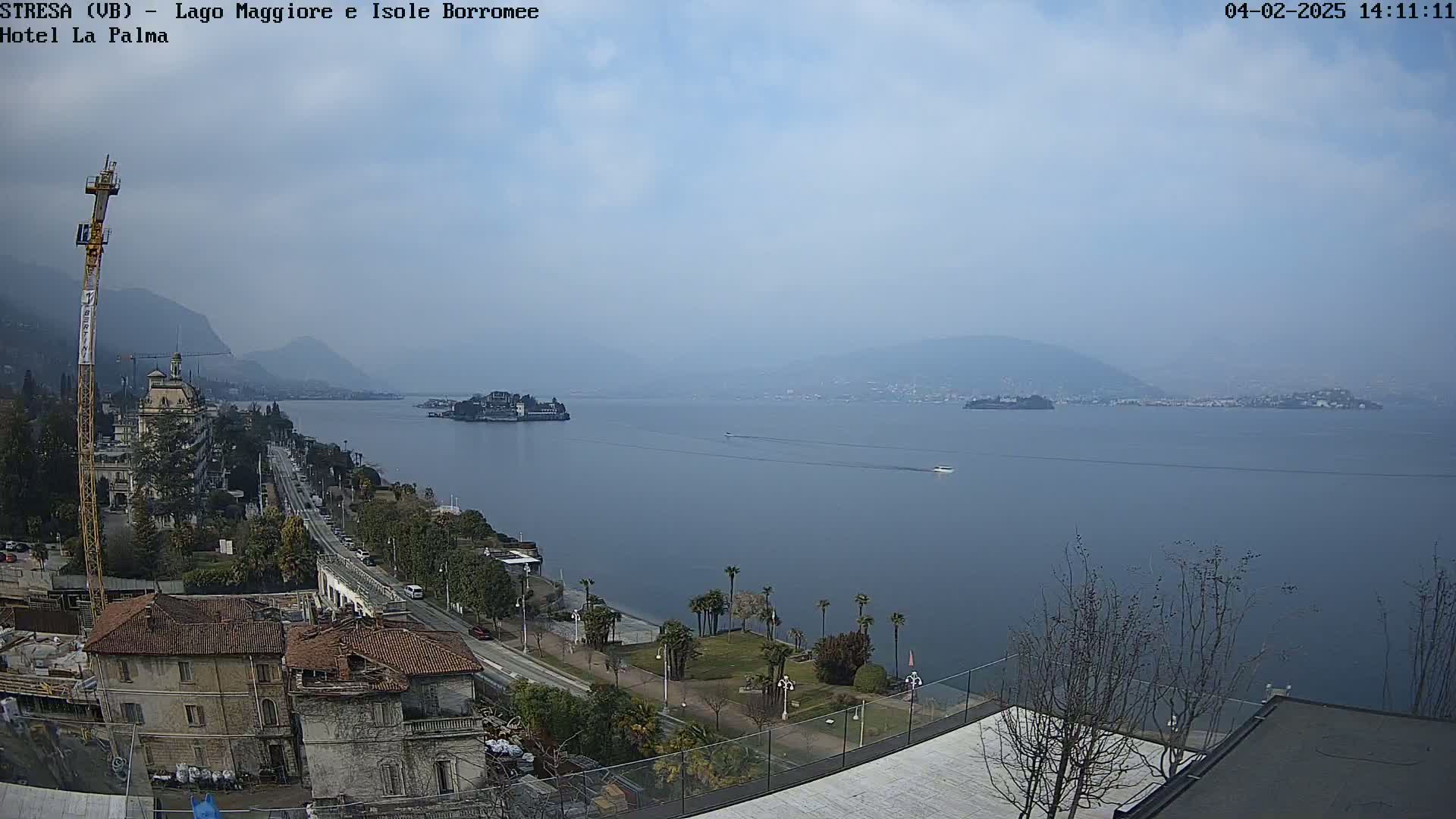 A hazy view of a lake with islands and mountains in the distance, showing a town with buildings and a road along the shoreline.