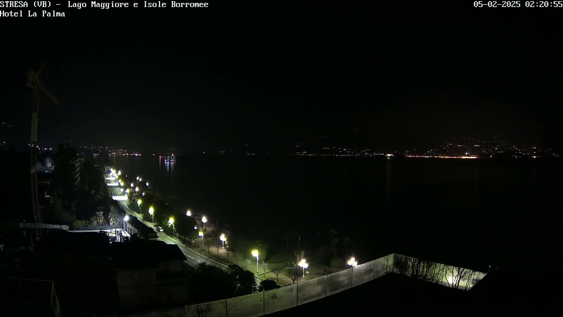 A nighttime view of a dark body of water with a shoreline illuminated by streetlights, a road, and distant city lights.