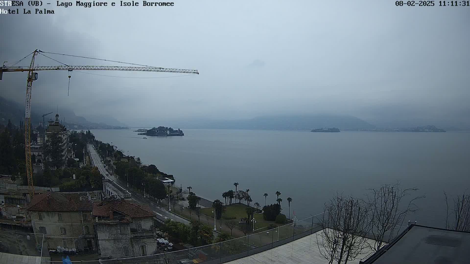A hazy, overcast day reveals a large body of water with islands in the distance, a shoreline with buildings and vegetation, and a construction crane visible in the foreground.