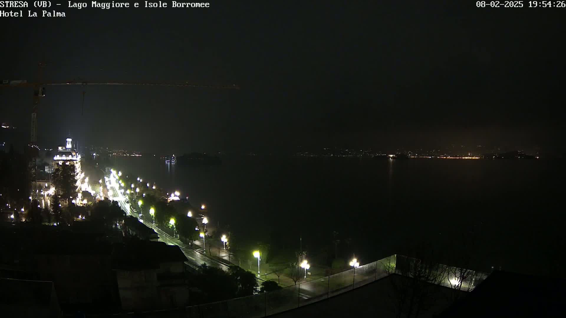 A nighttime view of a city street illuminated by streetlights alongside a dark body of water, under a hazy sky.