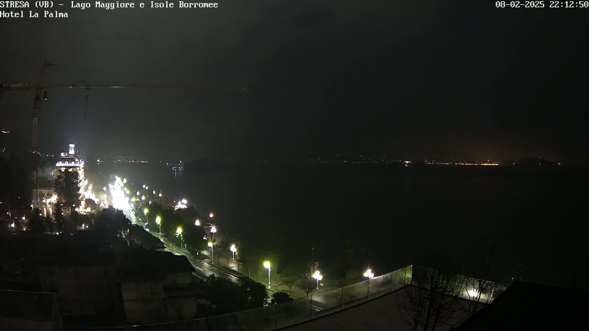 A nighttime, rainy view of a city along a body of water, with a construction crane and lit-up roads visible.