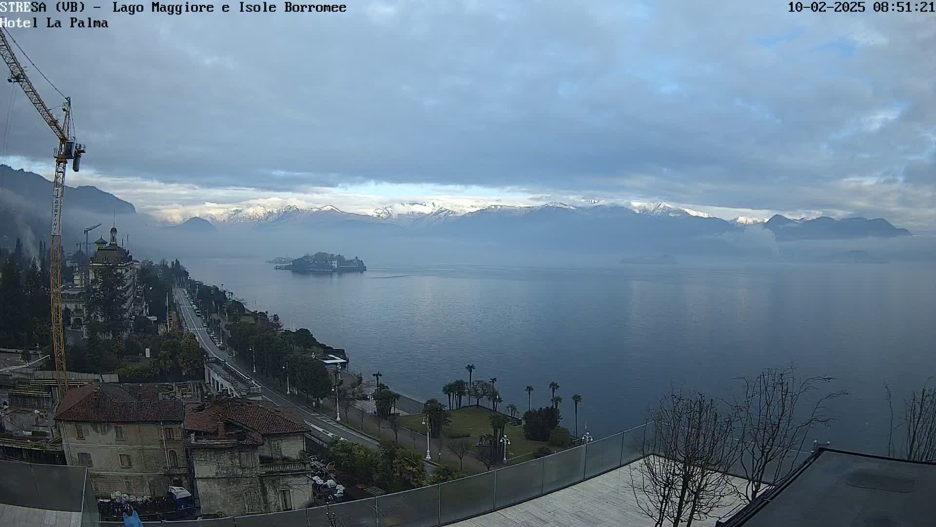 A hazy, overcast day reveals a cityscape overlooking a large lake with snow-capped mountains in the distance.