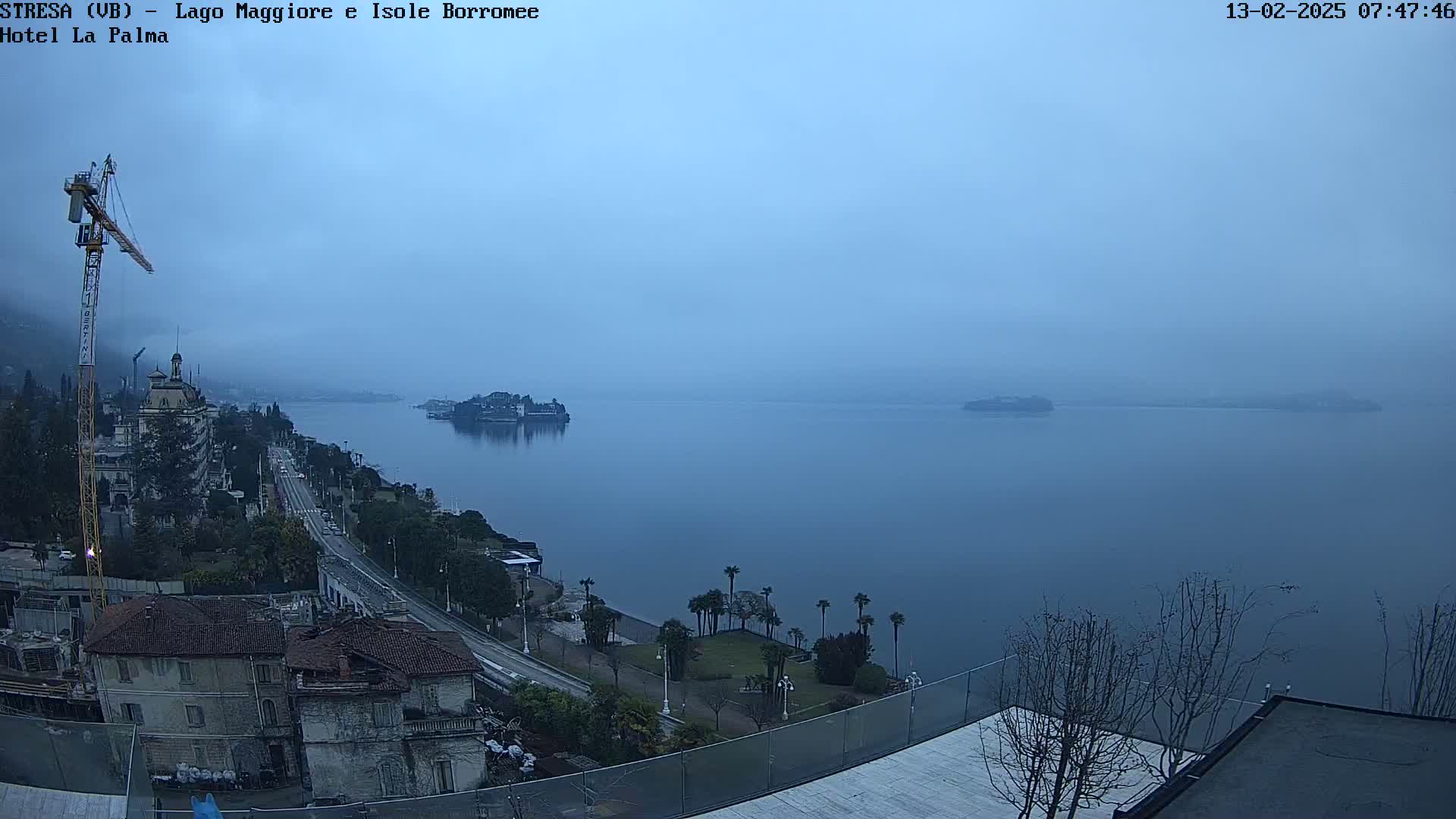 A foggy morning view overlooking a lake with islands in the distance, a shoreline with buildings and a road, and a construction crane nearby.