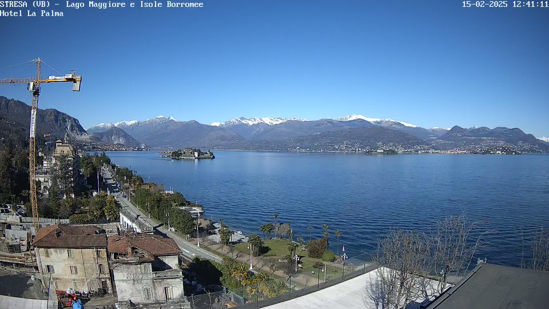 A sunny day overlooking a large lake with snow-capped mountains in the background, a construction crane, and buildings along the shoreline.