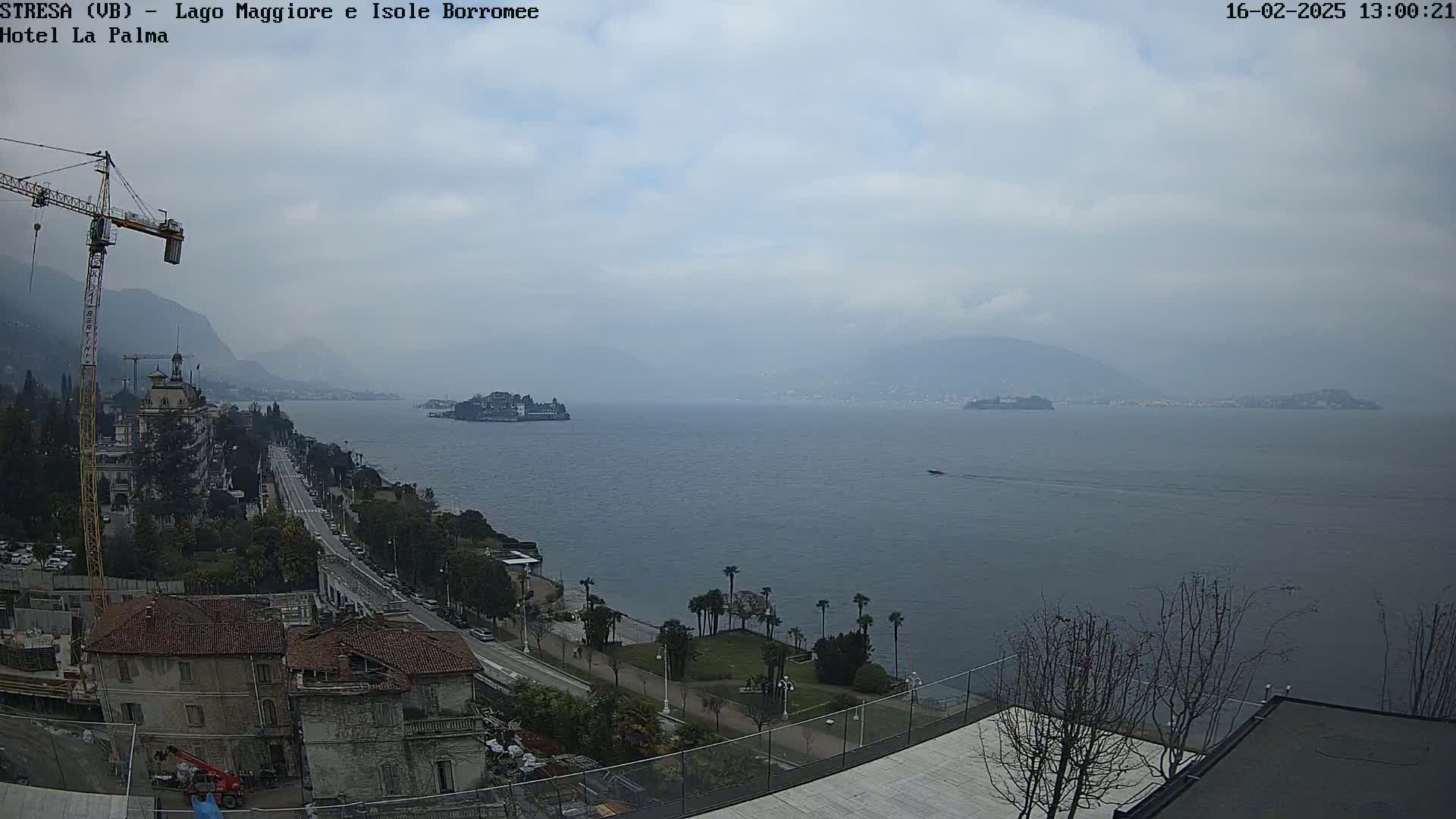 A hazy, overcast day reveals a large body of water with islands in the distance, a shoreline with palm trees and buildings, and a construction crane.