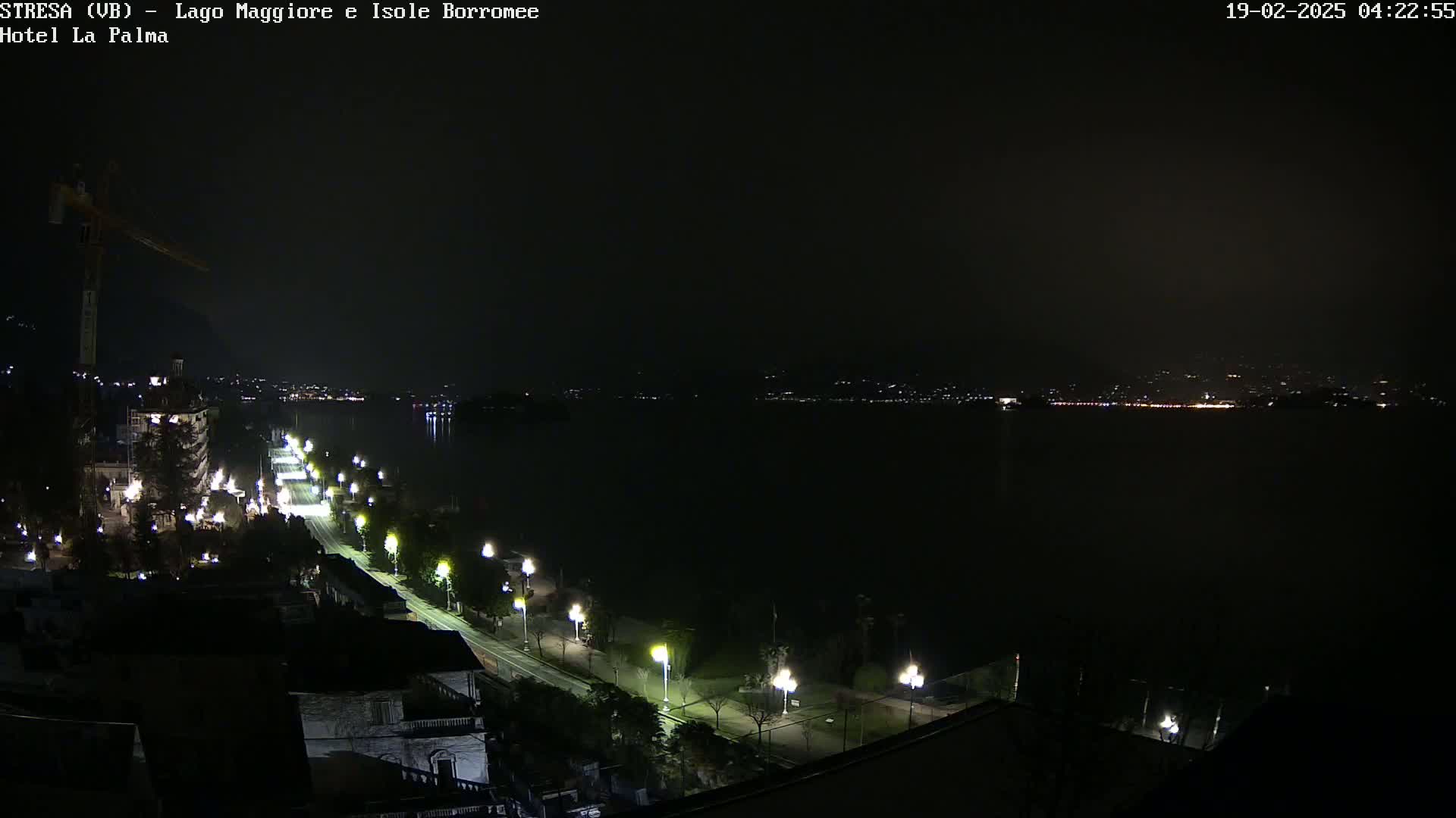 A nighttime view of a city beside a dark lake, illuminated by streetlights along a road and distant city lights across the water.